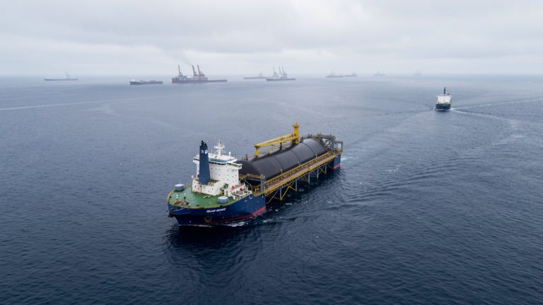 Vue aérienne réaliste d’une plateforme offshore danoise en mer du Nord, avec un navire transportant du CO2 liquéfié et des installations industrielles visibles au loin sous une lumière froide.
